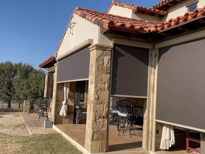 Three dark screens at different heights between Texas stone columns under a red tile roof, live oaks behind.