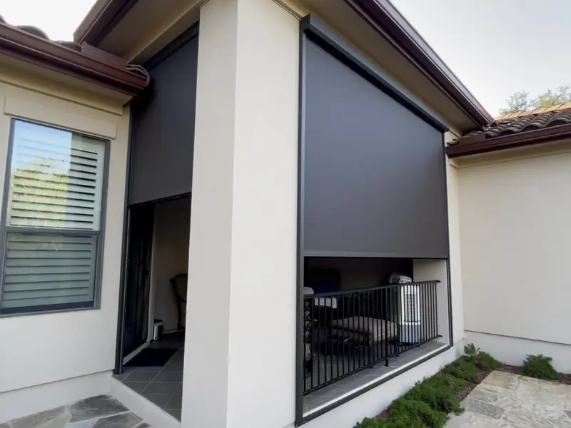 A stucco home with a tile roof, two dark screens lowered over an entry and a balcony.